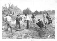 Young men working in field with hoes.