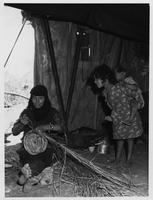 A mother and two children weave baskets.